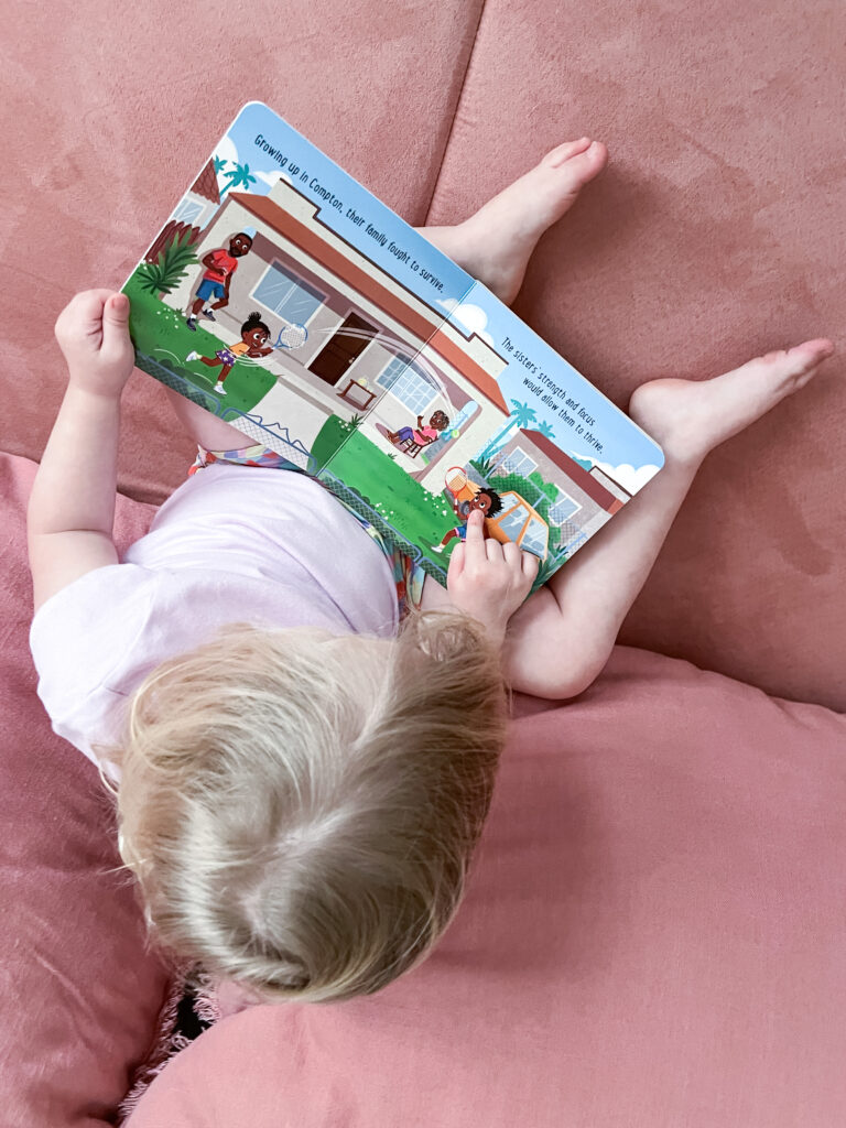 Child pointing to picture of girl playing tennis in board book Baby Ballers: Venus and Serena Williams